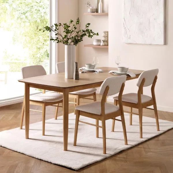 Dining room with wooden table and chairs on a white rug, natural light coming through windows.