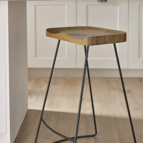 Wooden stool with metal legs in a room with white paneled walls and wooden floor.