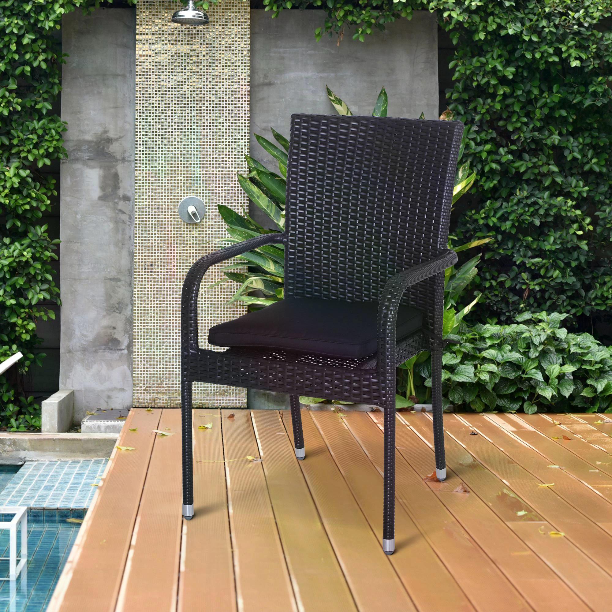Black wicker chair with a cushion on a wooden deck by a poolside.