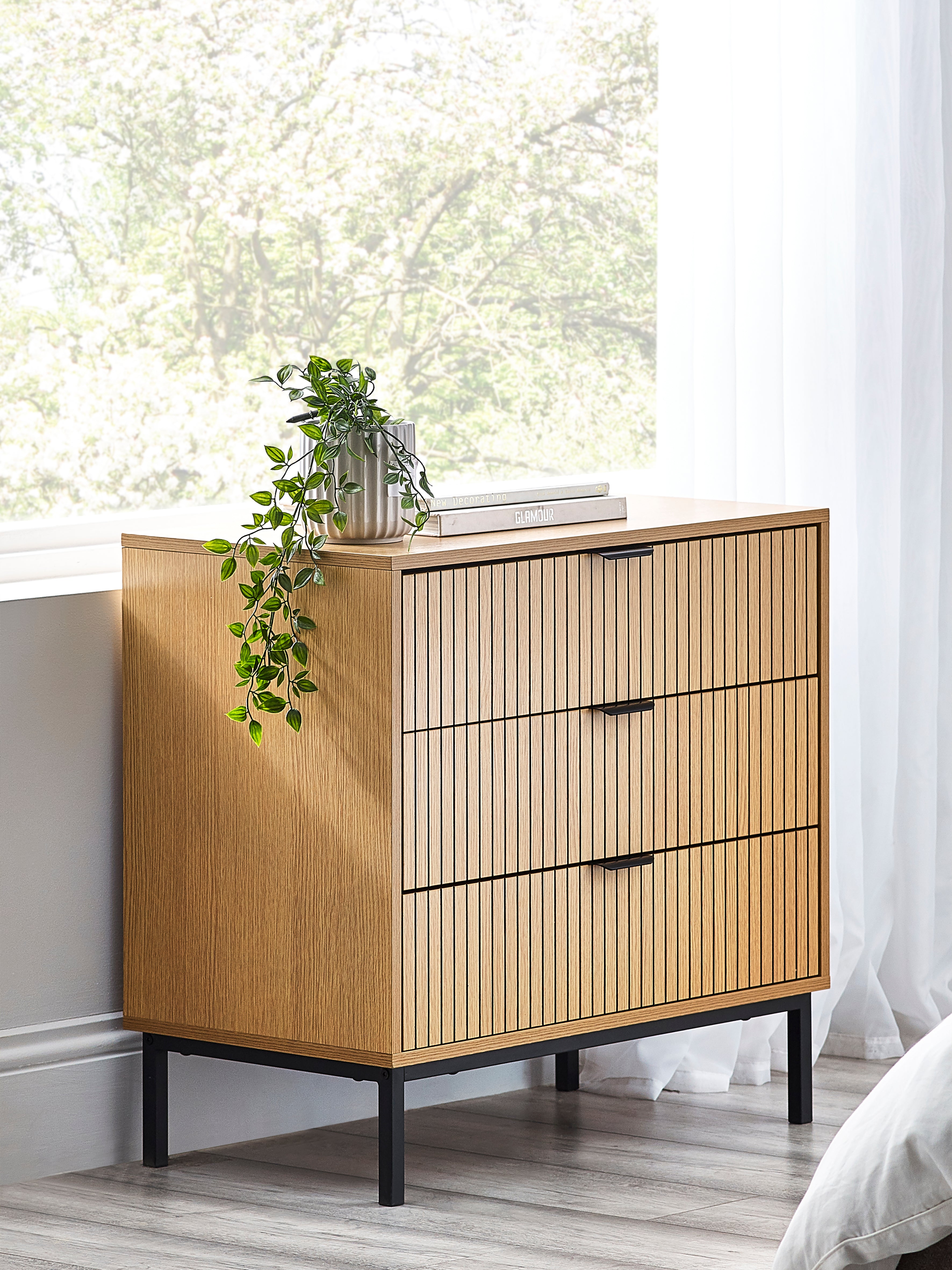 Wooden dresser with black legs and decorative elements in a bright room.