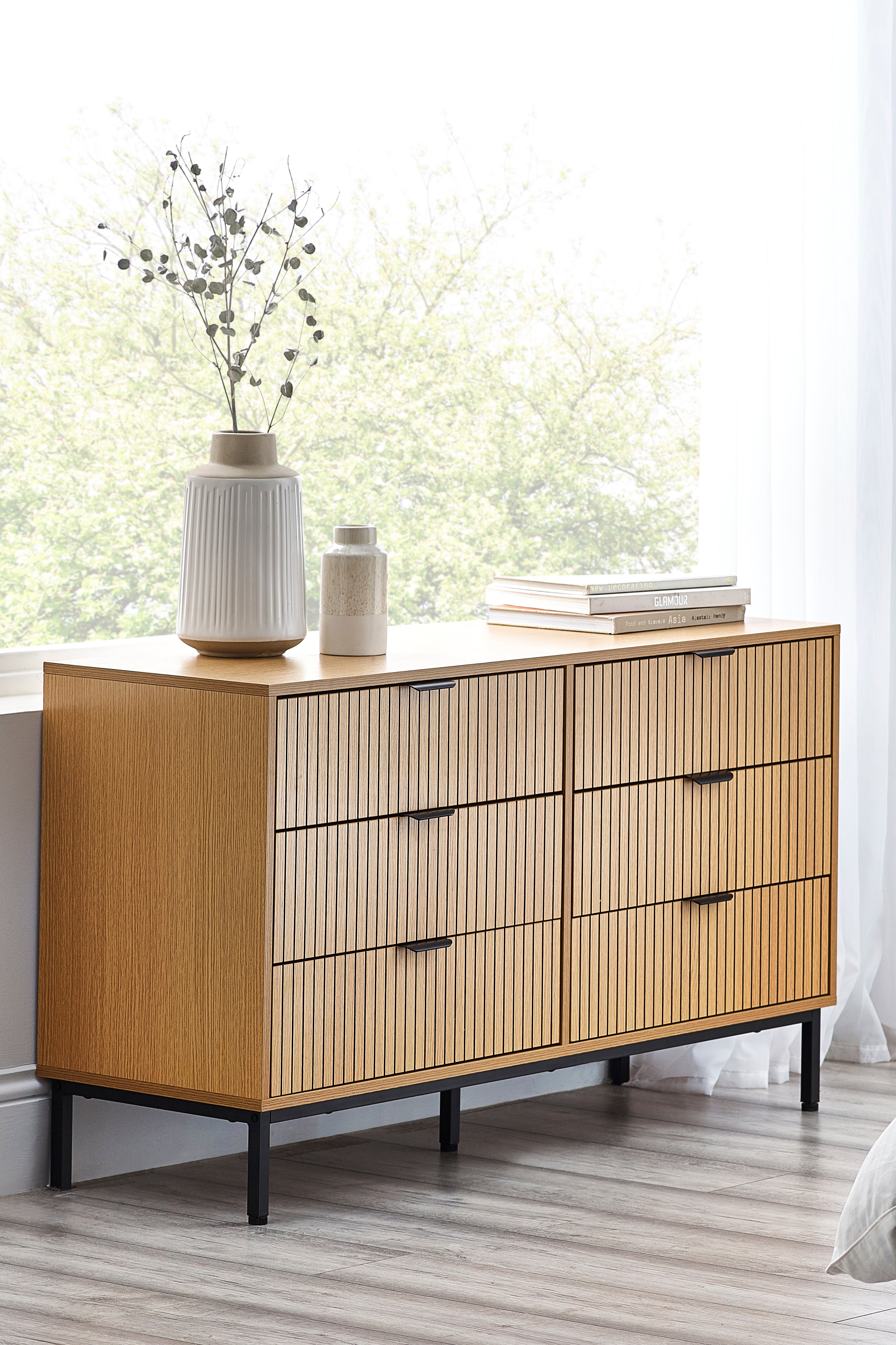 Wooden dresser with black handles in a room with a window and decor items.