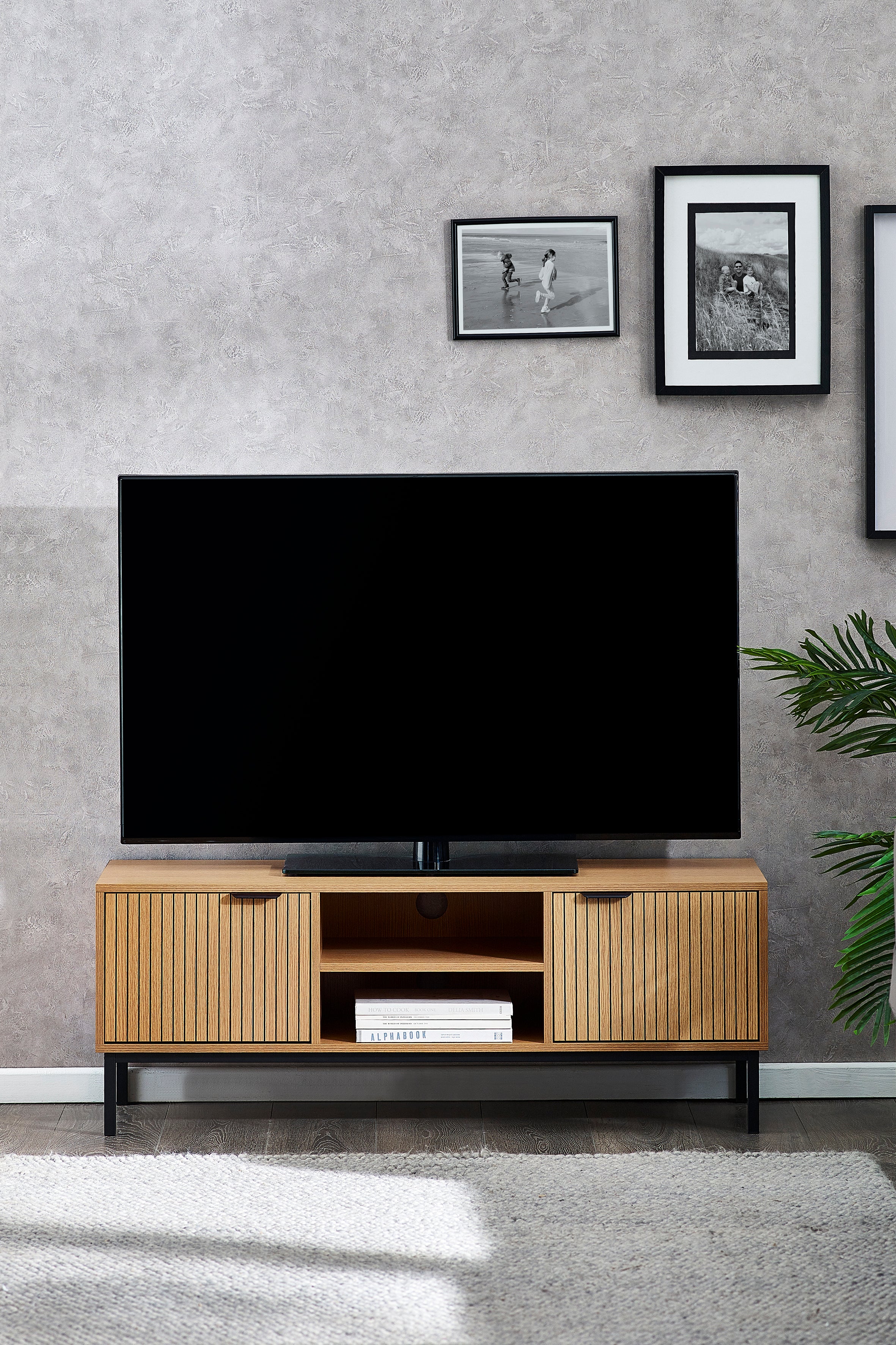 TV on a wooden stand against a gray wall with framed pictures.