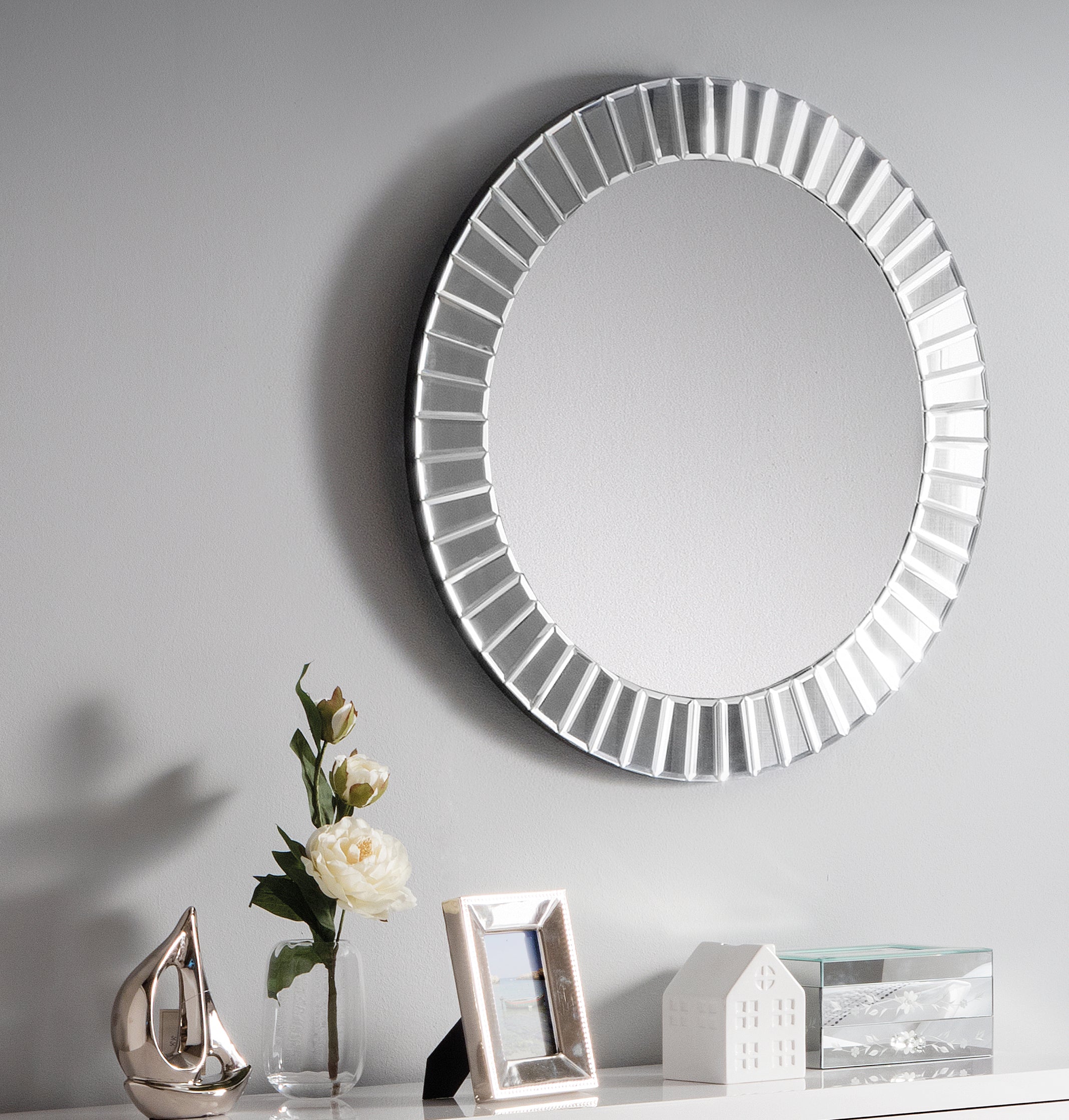 Round decorative mirror with a ribbed frame on a gray wall, with a small table displaying decorative items.
