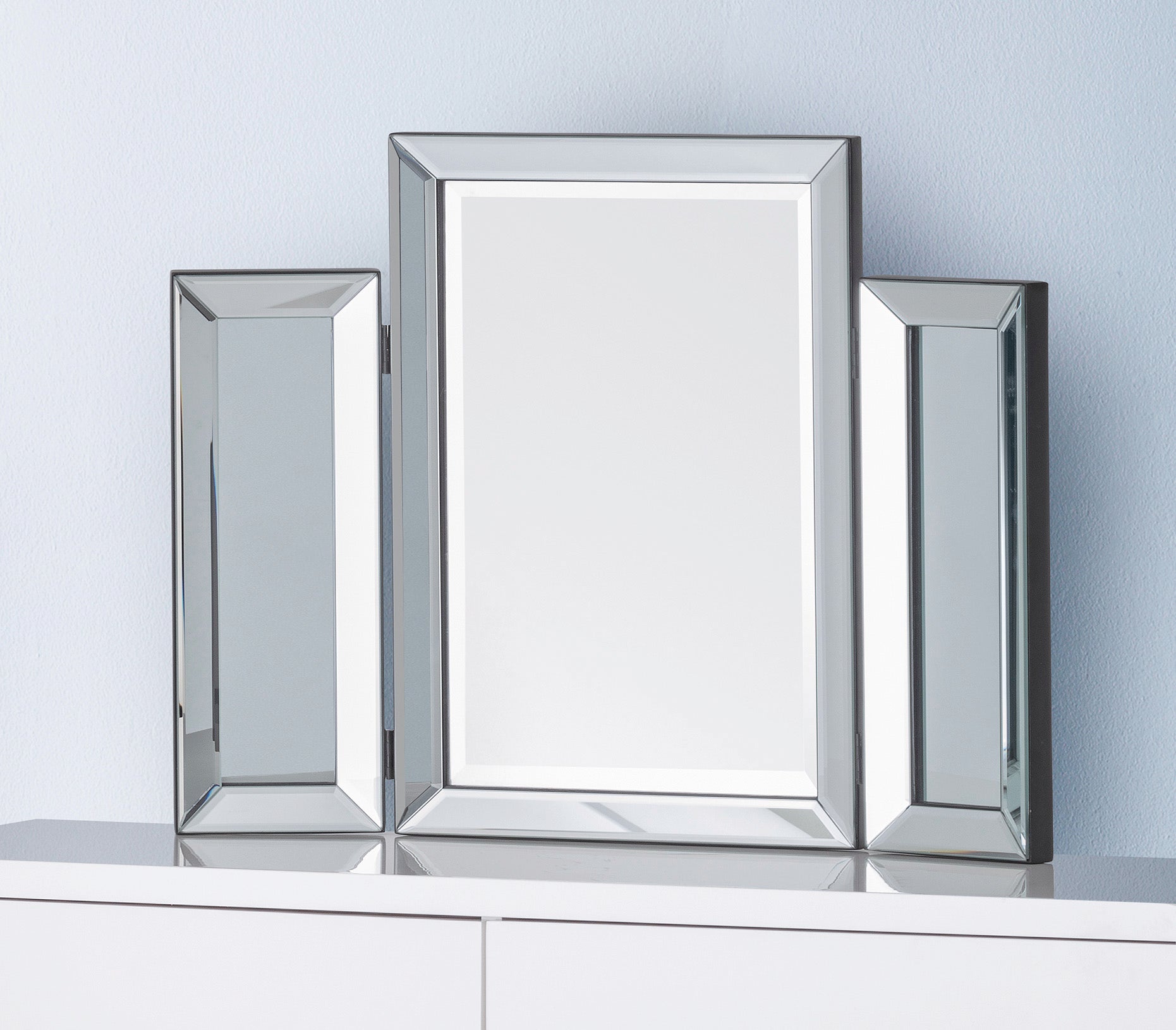 Three silver-framed mirrors of different sizes on a white surface with a light blue wall background.