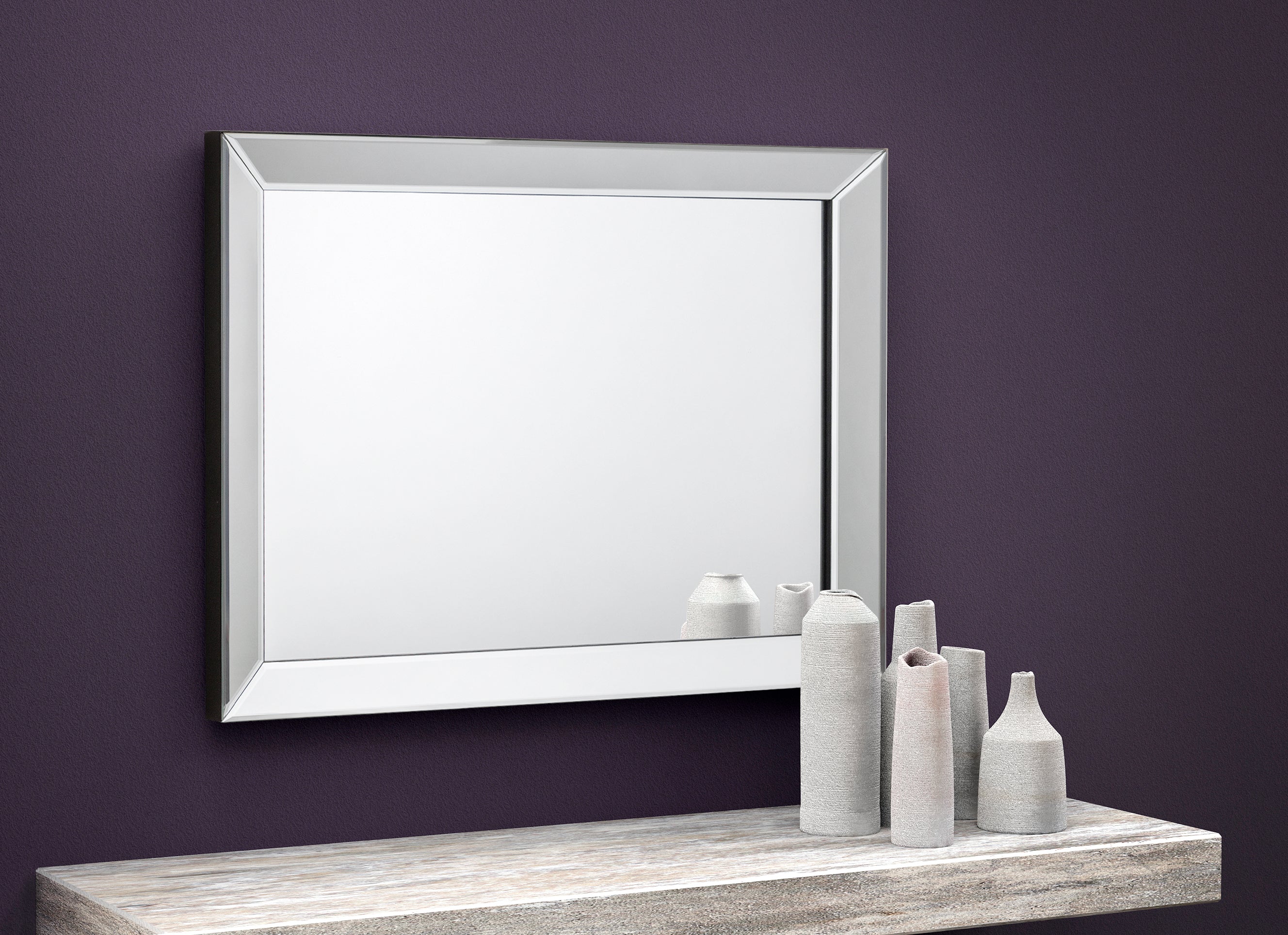 Silver-framed mirror on a purple wall with decorative vases below