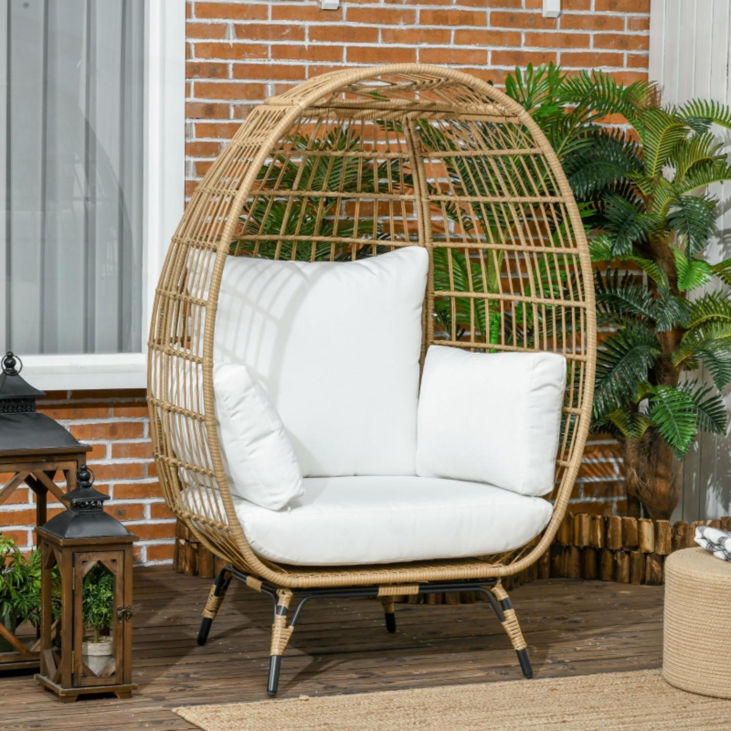 Wicker egg-shaped chair with white cushions on a wooden deck with plants and lanterns.