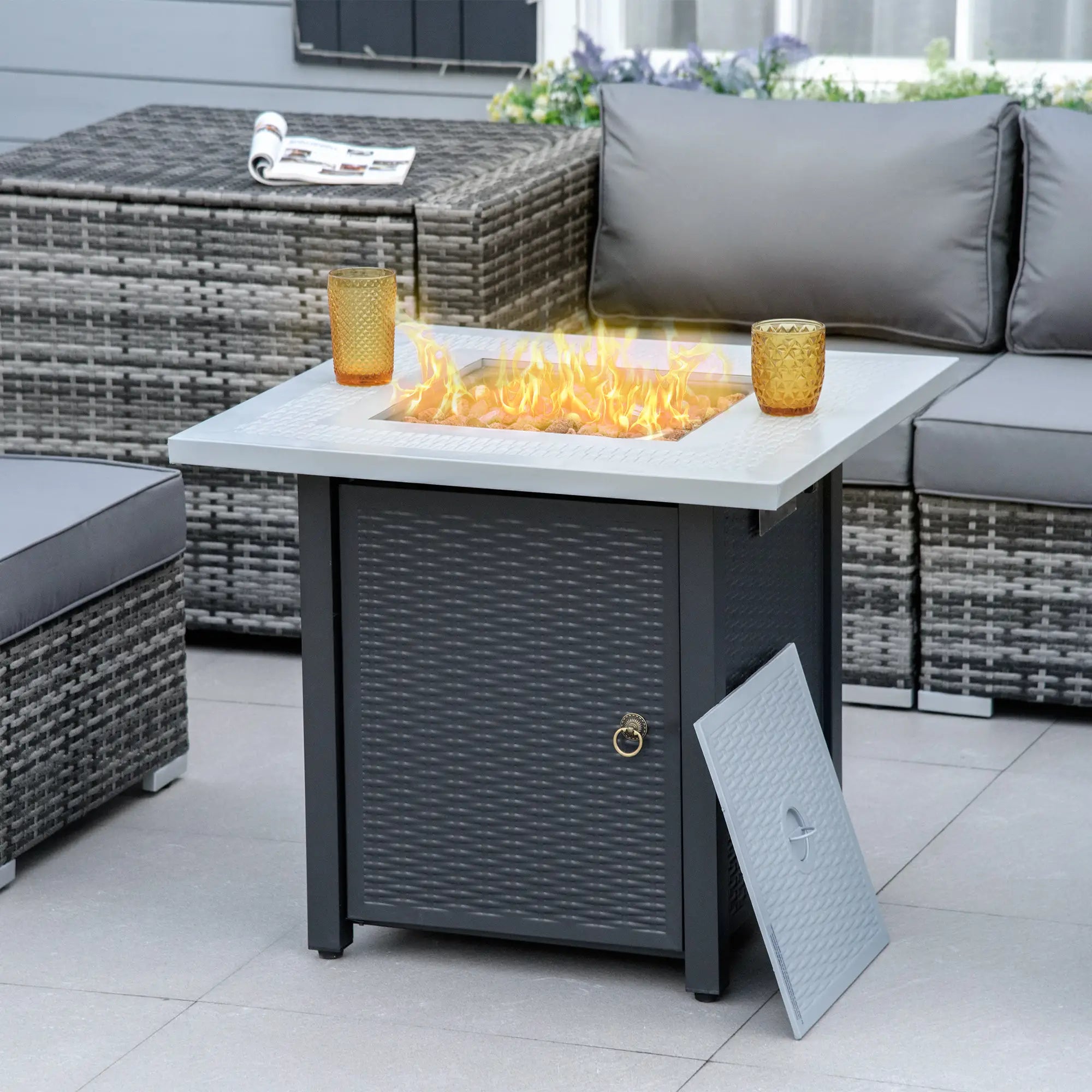 Outdoor patio with fire pit table, gray sofa, and wicker chairs.