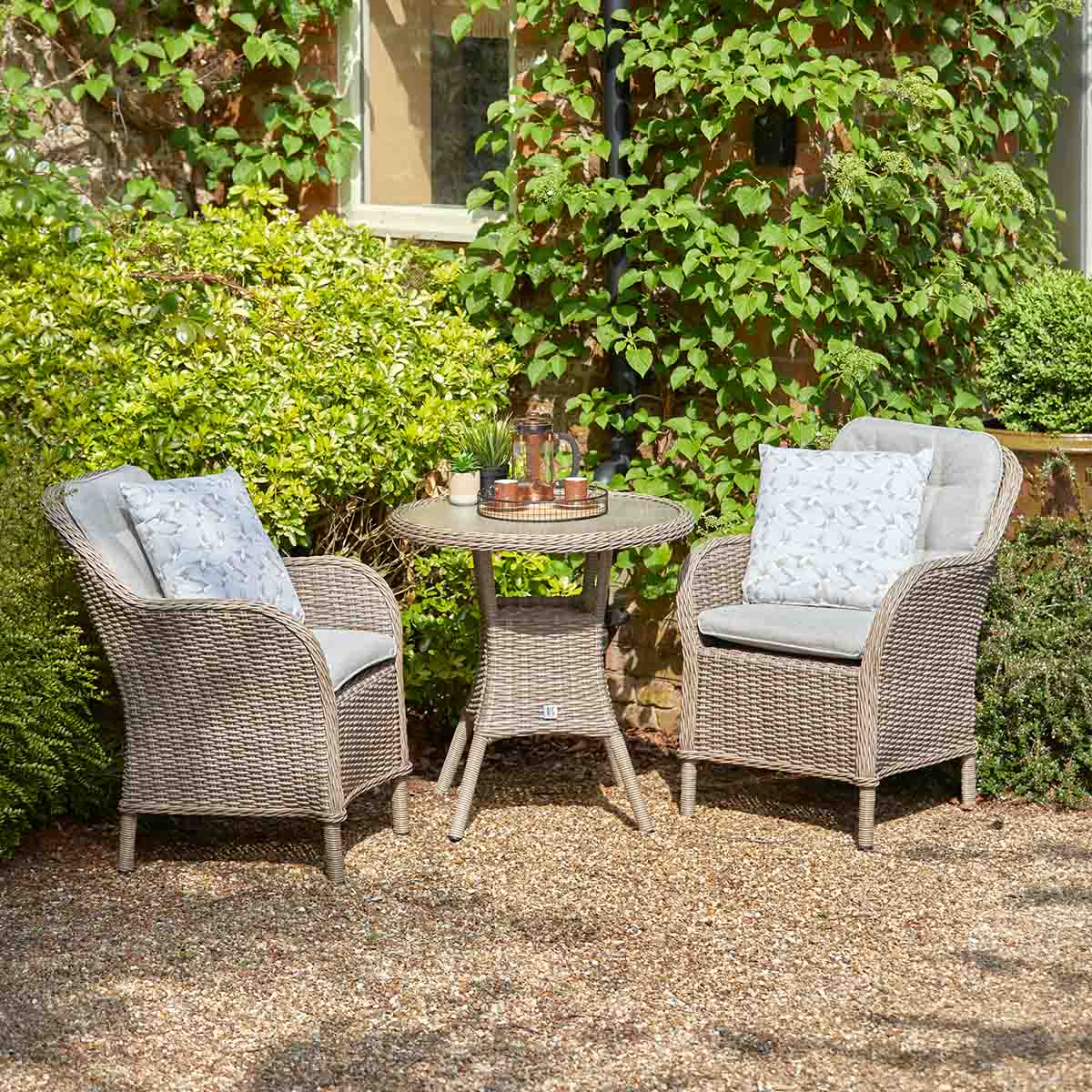 Two wicker chairs with cushions and a small table in a garden setting.