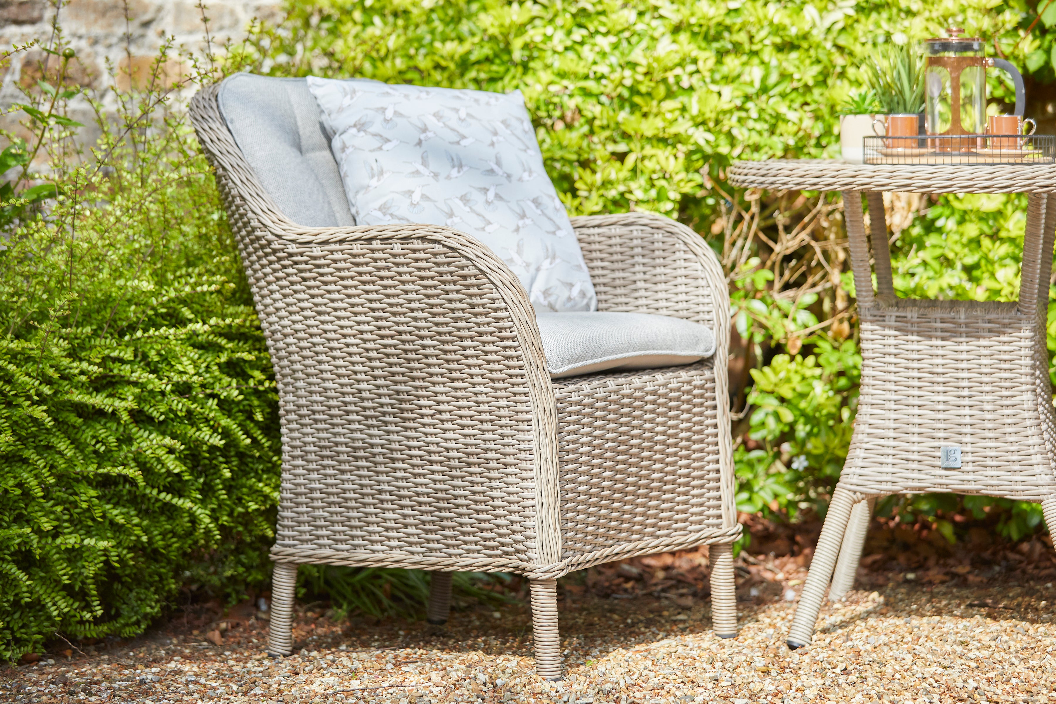 Wicker chair with cushions and a matching table in a garden setting