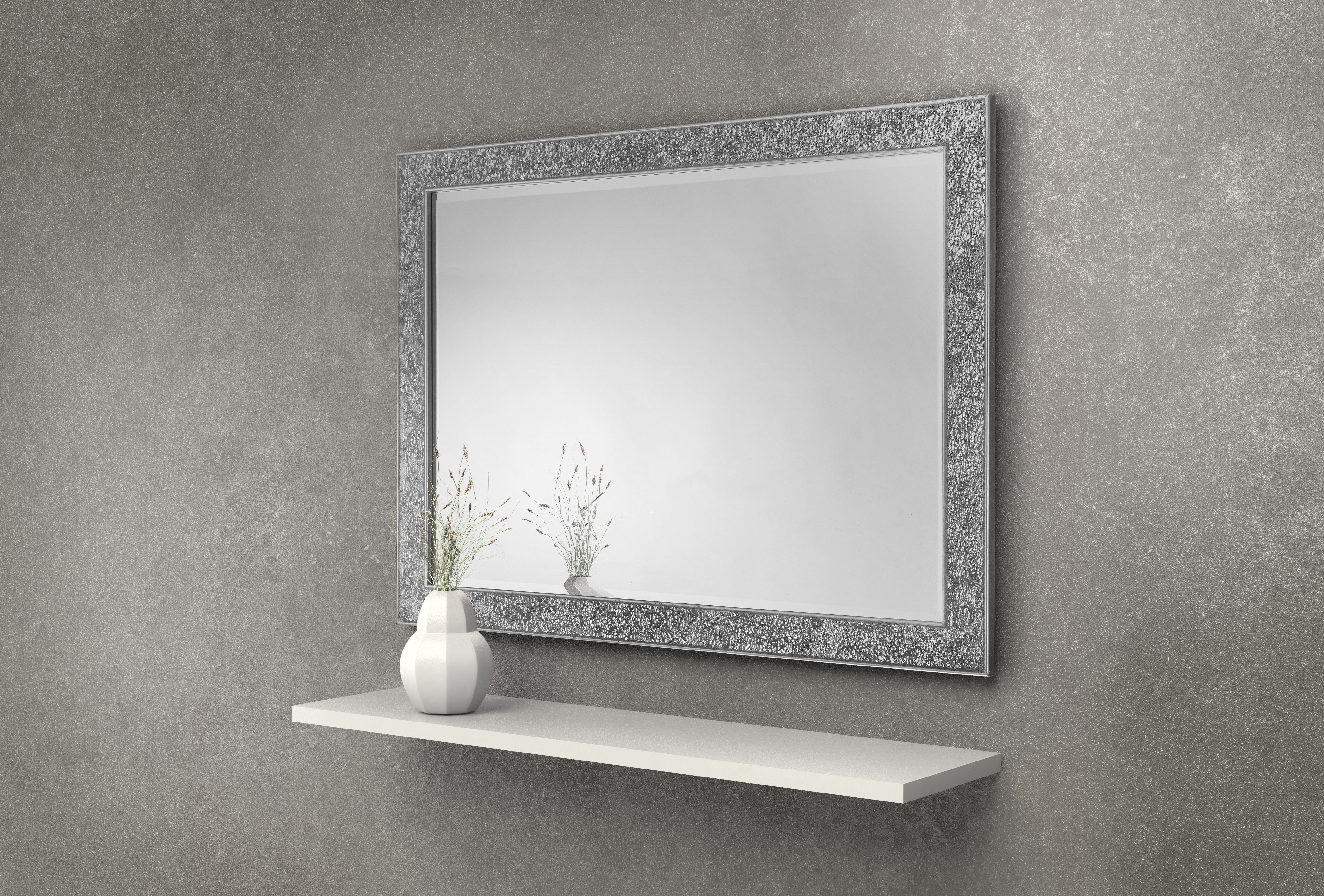 Decorative mirror with a textured frame on a gray wall above a white shelf.