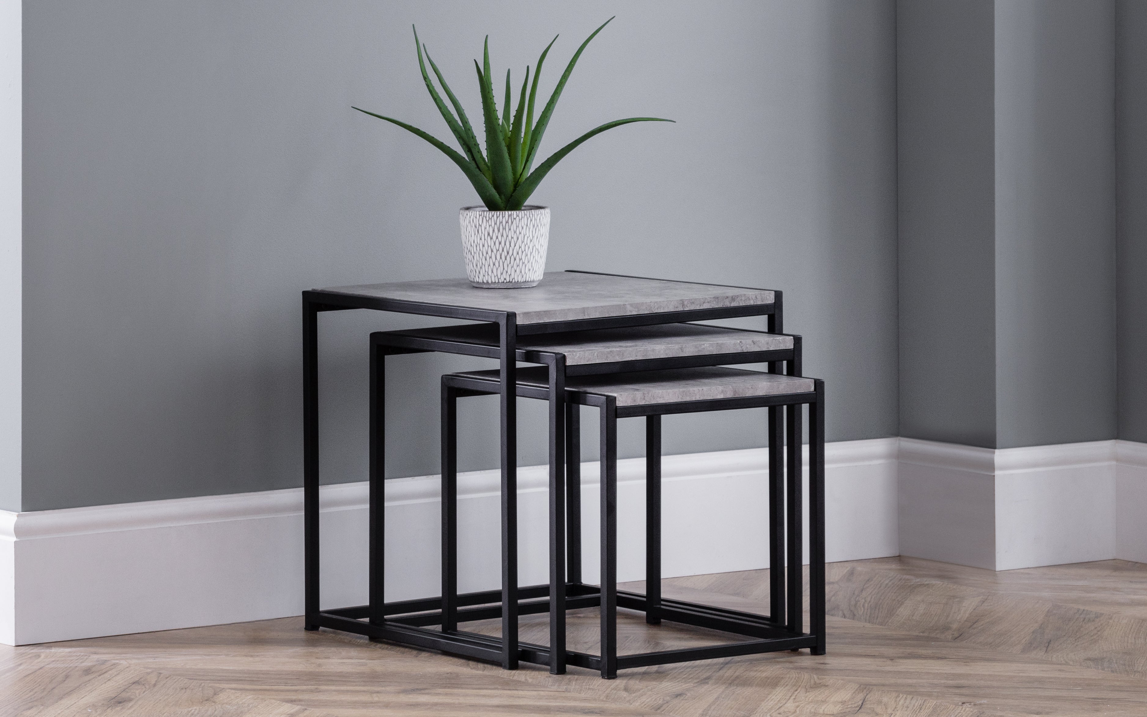 Set of three black metal nesting tables with a potted plant on a gray wall background
