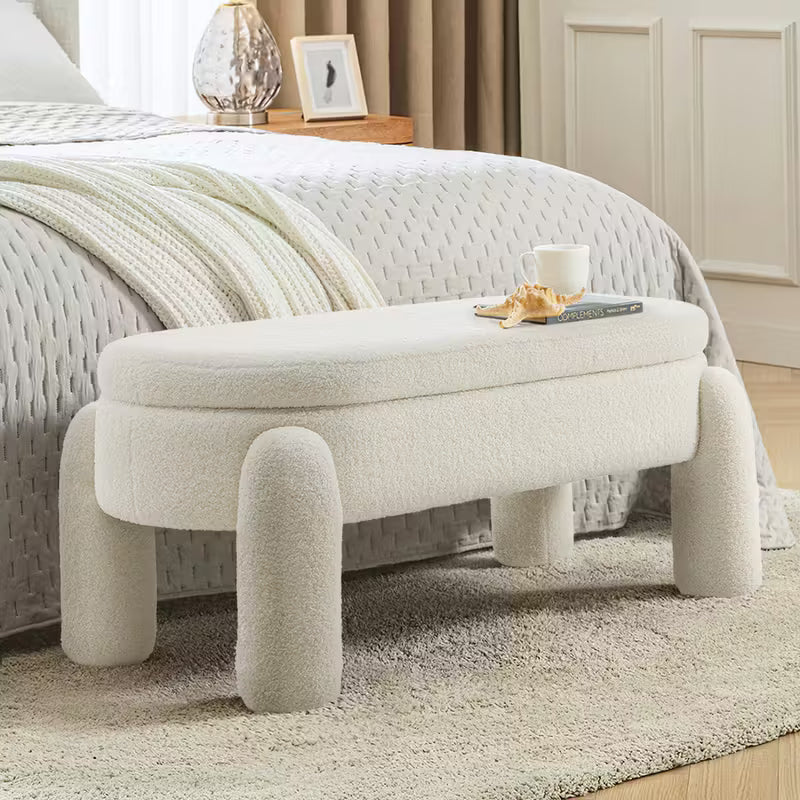 Beige upholstered storage bench positioned at the foot of a bed in a minimalist bedroom