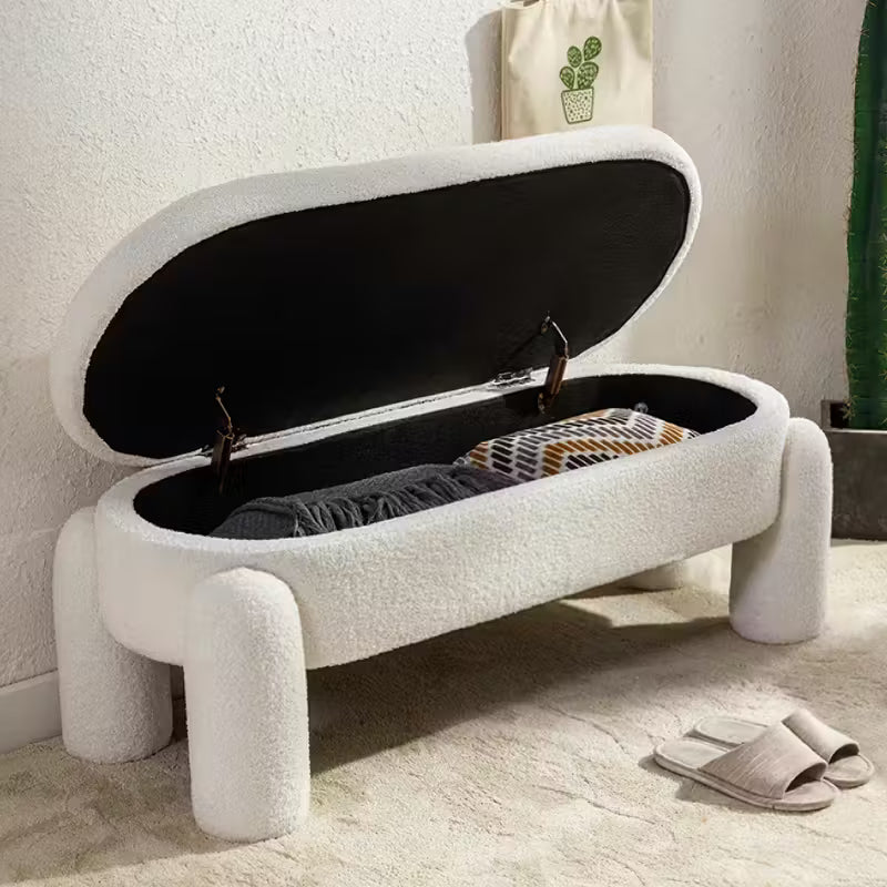 White storage bench with open lid revealing clothes, placed against a light wall.