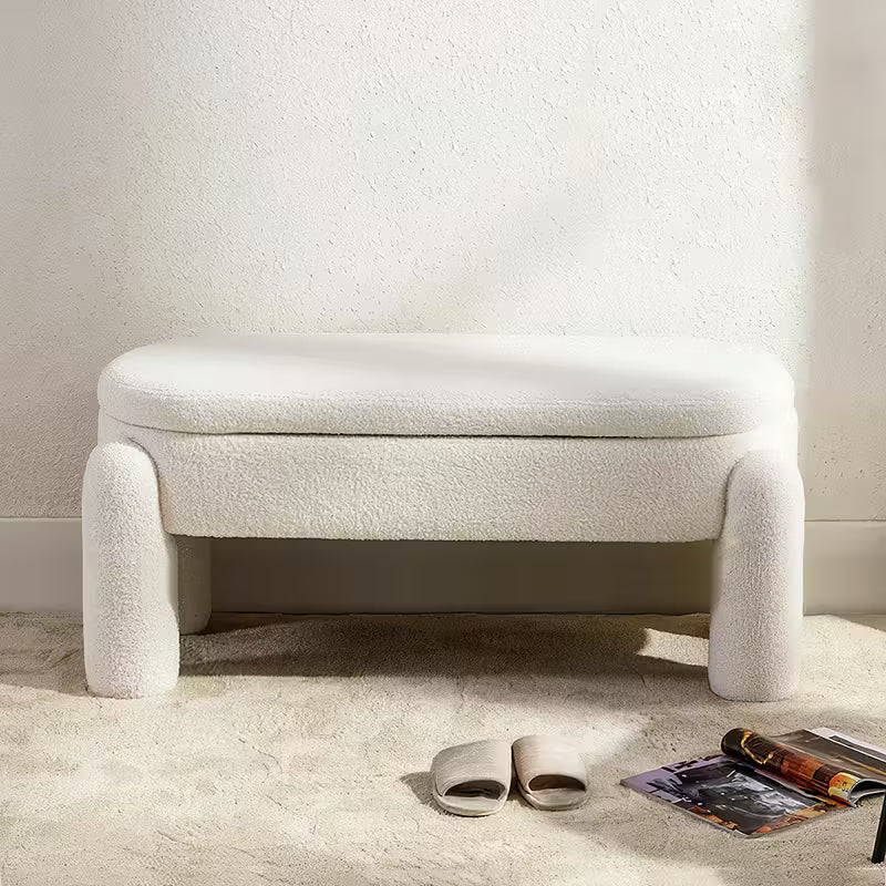 Beige upholstered bench in a minimalistic room with a magazine and sandals on the floor.