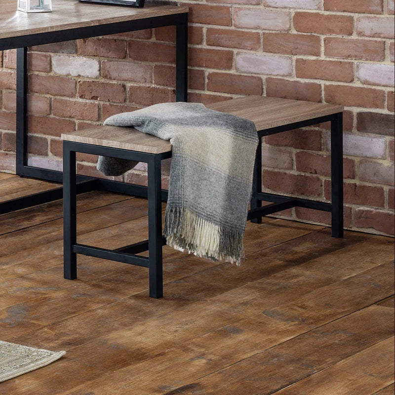 Wooden bench with a blanket draped over it against a brick wall.