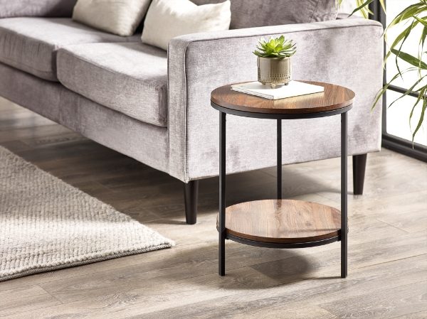 Round wooden side table with metal legs in a living room setting.