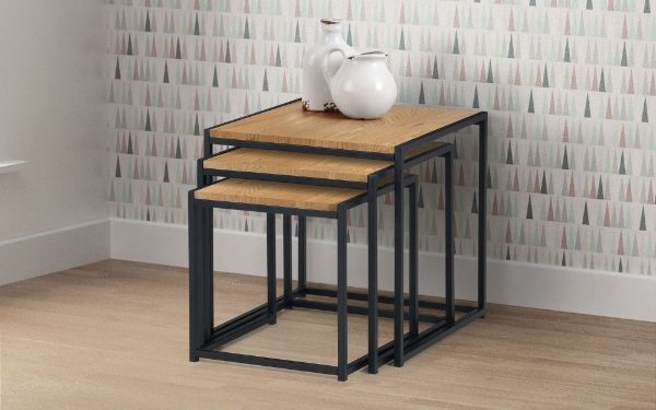 Set of three nesting tables with wooden tops and black metal frames against a patterned wall.