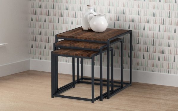Set of three nesting tables with a wooden finish and black metal legs against a patterned wall.