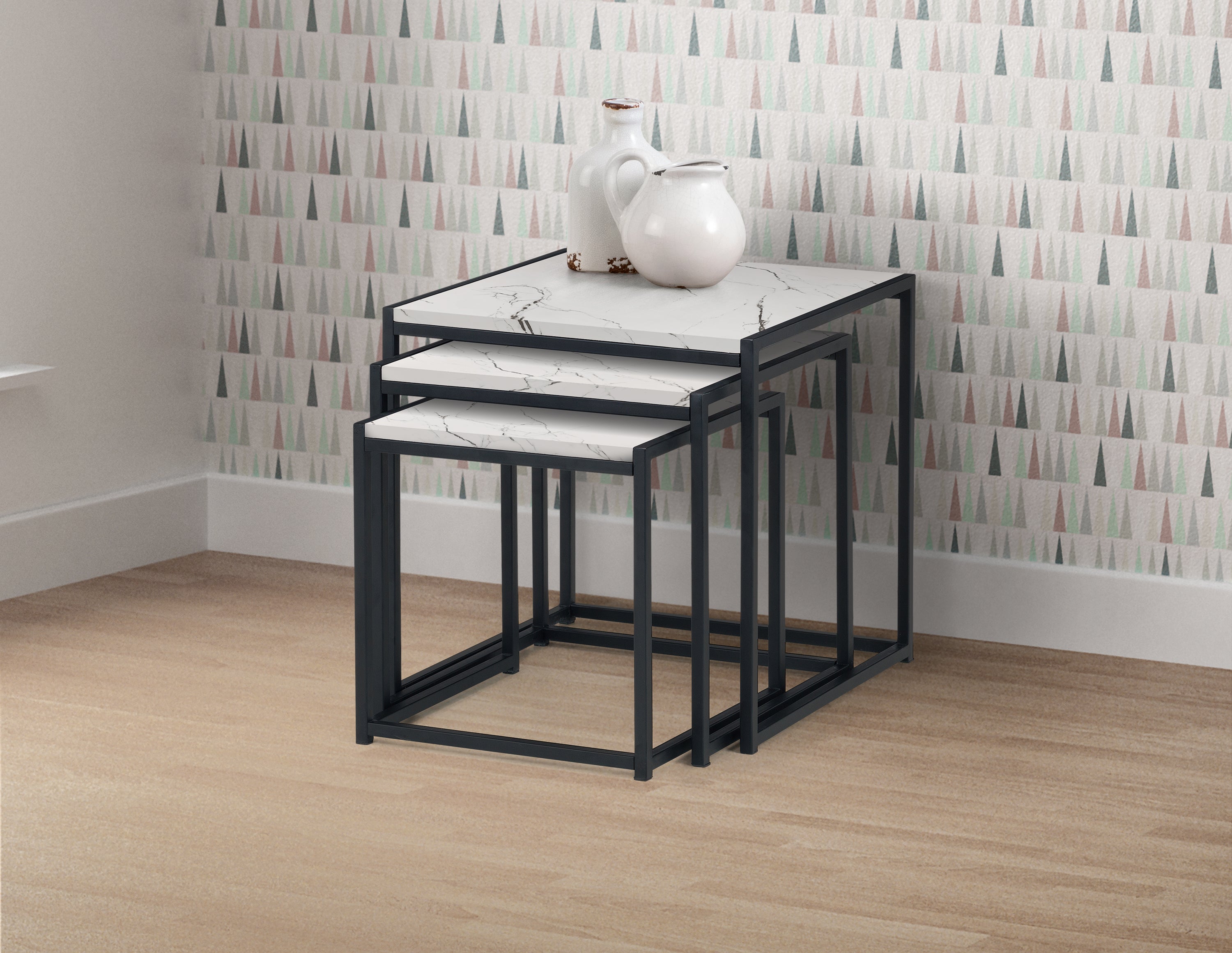 Set of three nesting tables with marble top and black metal frame against a patterned wall.