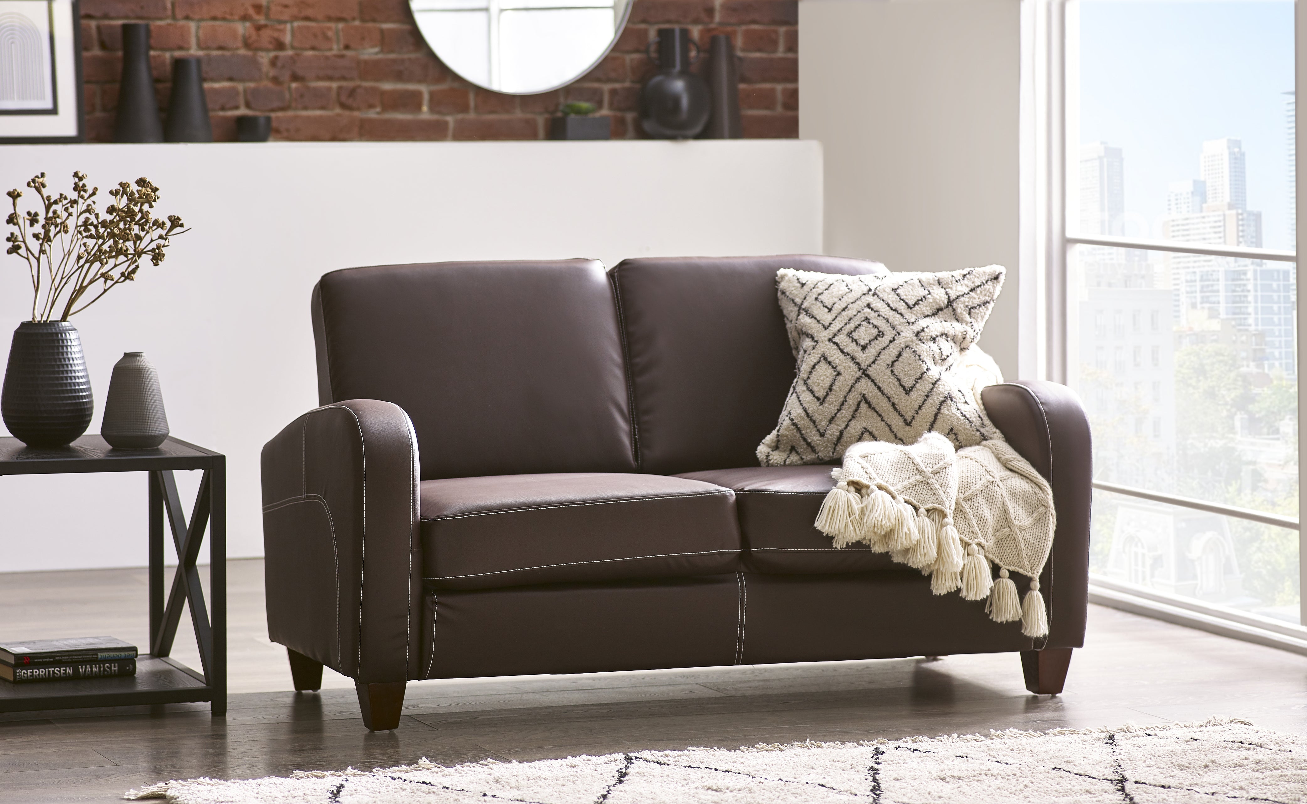 Brown leather sofa with decorative pillows and a blanket in a living room setting.