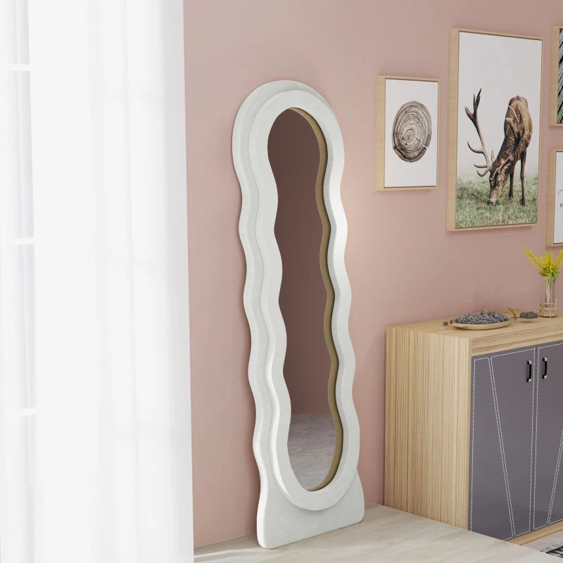 White wavy floor mirror in a room with pink walls and a cabinet.