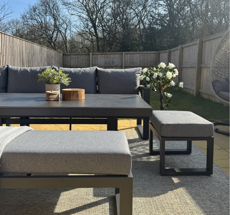 Outdoor patio set with gray cushions and a wooden table in a backyard setting.