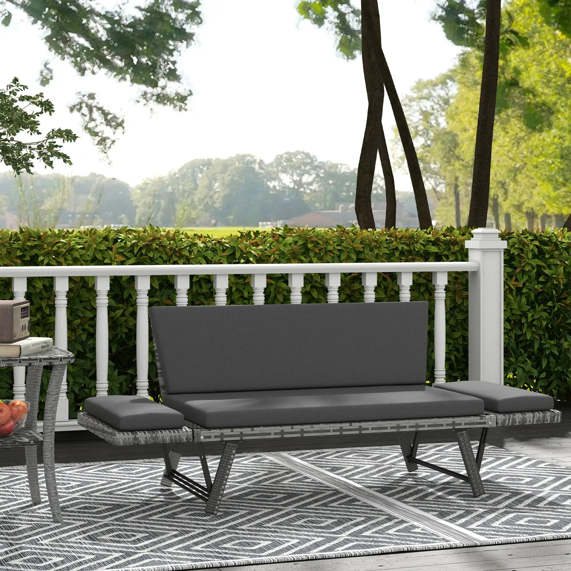Gray outdoor sofa on a deck with a white railing and greenery in the background
